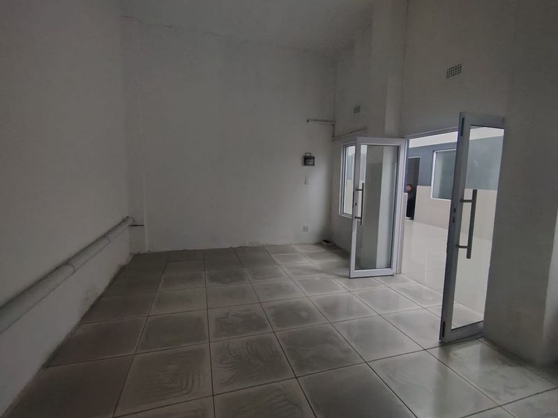 An empty, utilitarian space featuring tiled flooring, exposed conduit, and an aluminium-framed glass door leading to an adjacent area.