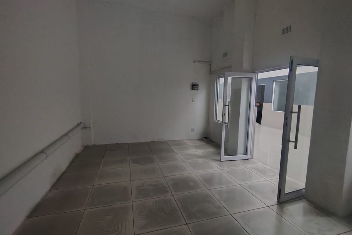 An empty, utilitarian space featuring tiled flooring, exposed conduit, and an aluminium-framed glass door leading to an adjacent area.