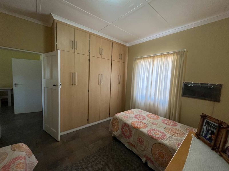 A functional bedroom featuring extensive floor-to-ceiling built-in cupboards, tiled flooring, and a wall-mounted air conditioning unit.
