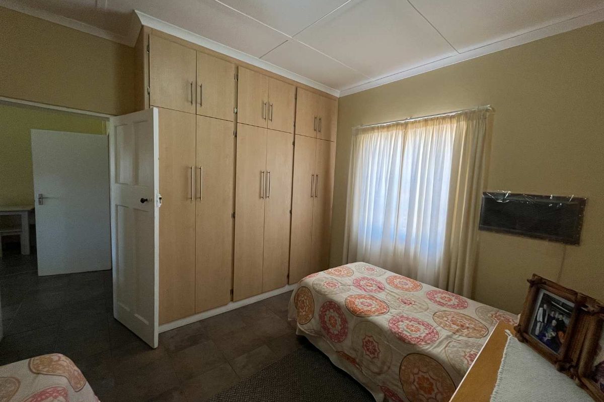 A functional bedroom featuring extensive floor-to-ceiling built-in cupboards, tiled flooring, and a wall-mounted air conditioning unit.