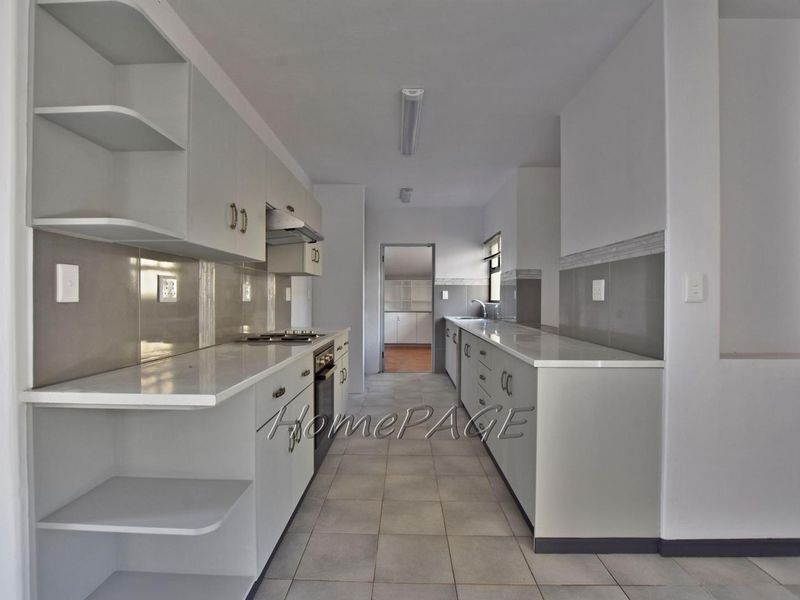A clean, galley-style kitchen featuring modern cabinetry, stone countertops, built-in oven, gas hob, and tiled flooring.