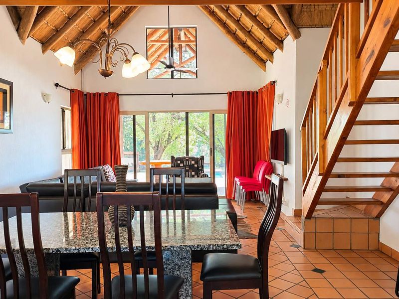 Spacious open-plan living and dining area featuring high vaulted thatched ceilings, exposed timber trusses, terracotta flooring, and a wooden staircase leading to an upper level.