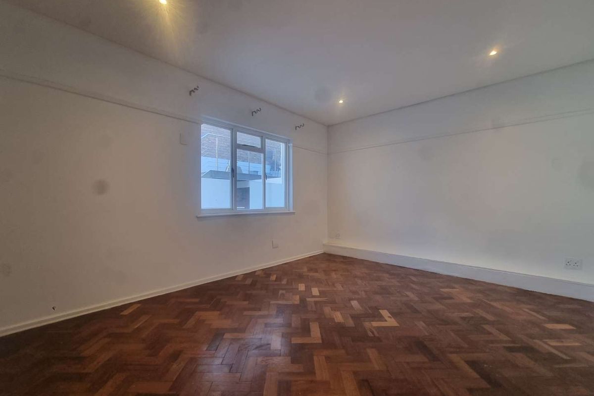 An empty bedroom featuring classic parquet flooring, recessed downlighting, and a picture rail, offering a blank canvas for personalization.