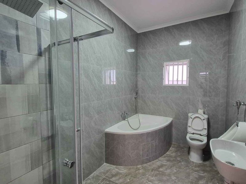 Modern bathroom featuring a glass-enclosed shower, a built-in bathtub, a pedestal basin, and a toilet, finished with contemporary grey wall and floor tiling.