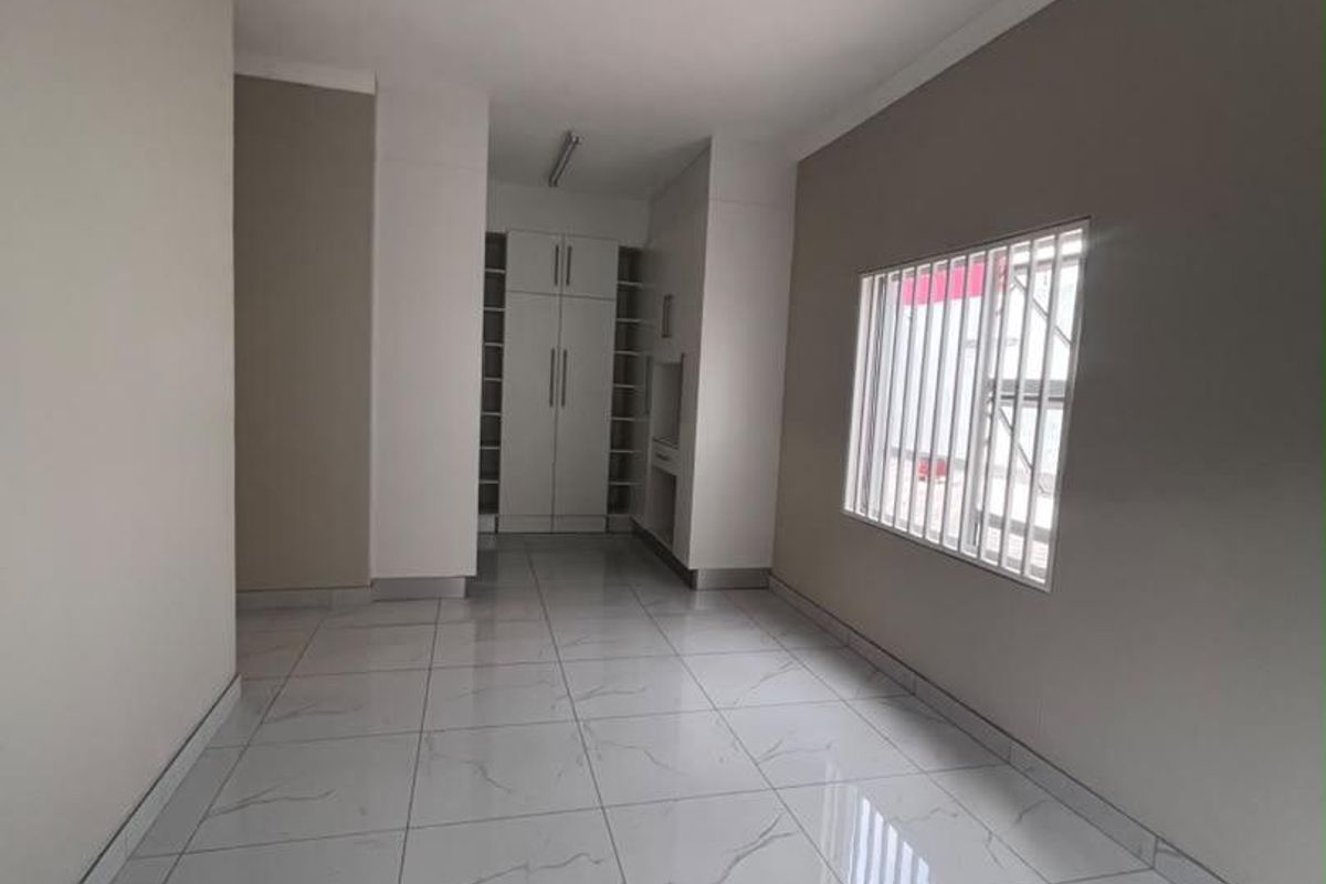 A bright, empty bedroom featuring modern marble-look tiled flooring, built-in cupboards, and a window fitted with security bars.