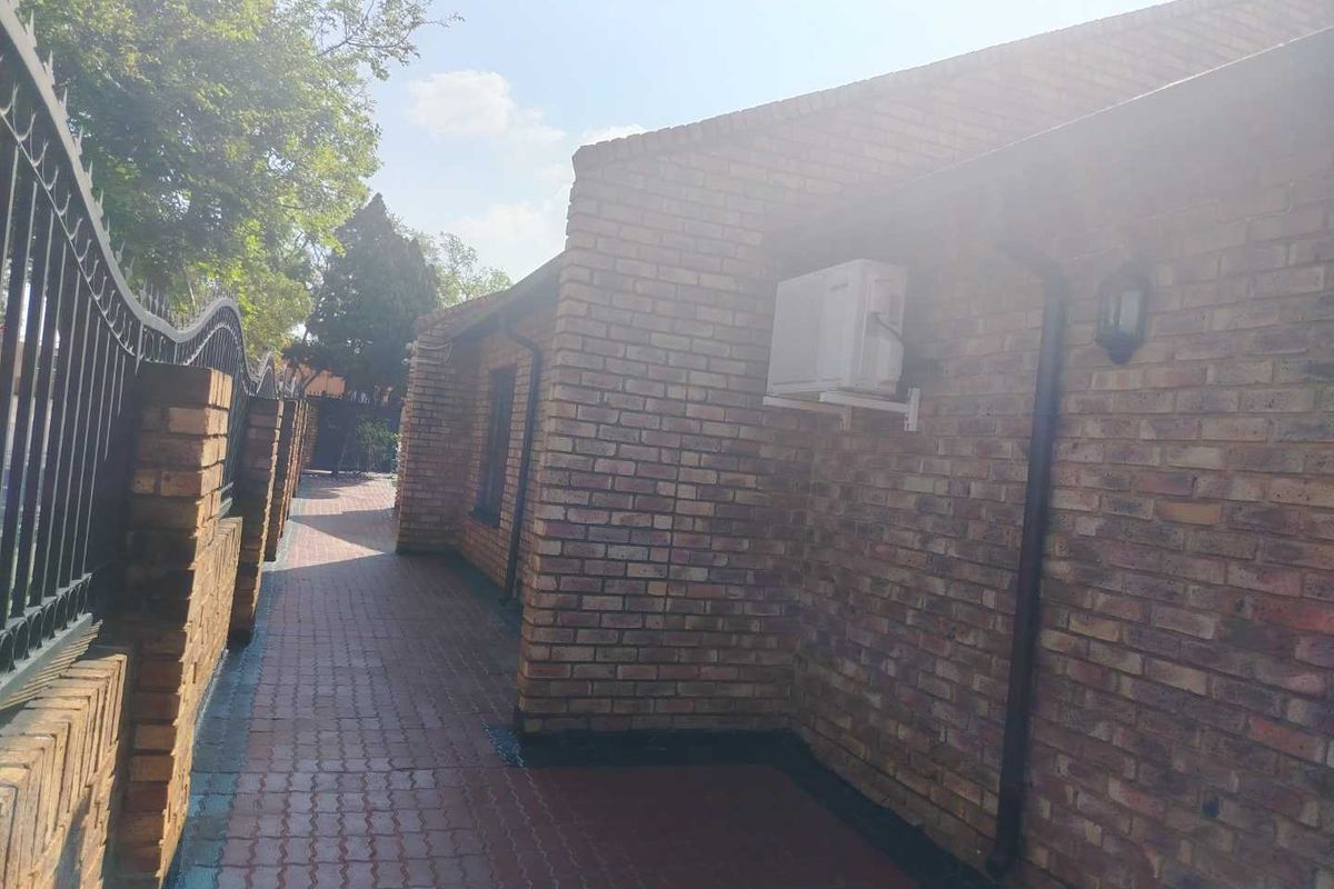 A side exterior view of the property featuring face brick walls, a paved walkway, and a secure wrought iron perimeter fence.
