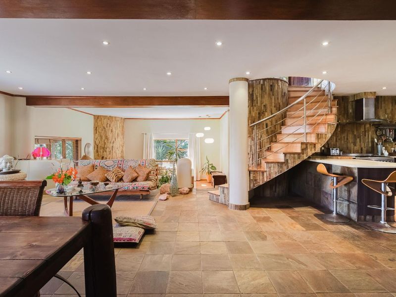 Spacious open-plan living area featuring a striking spiral staircase, stone tile flooring, and a modern kitchen with a breakfast bar and stone feature wall.