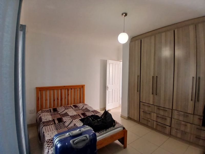 A bedroom featuring built-in wooden cupboards, tiled flooring, and a central pendant light fixture.