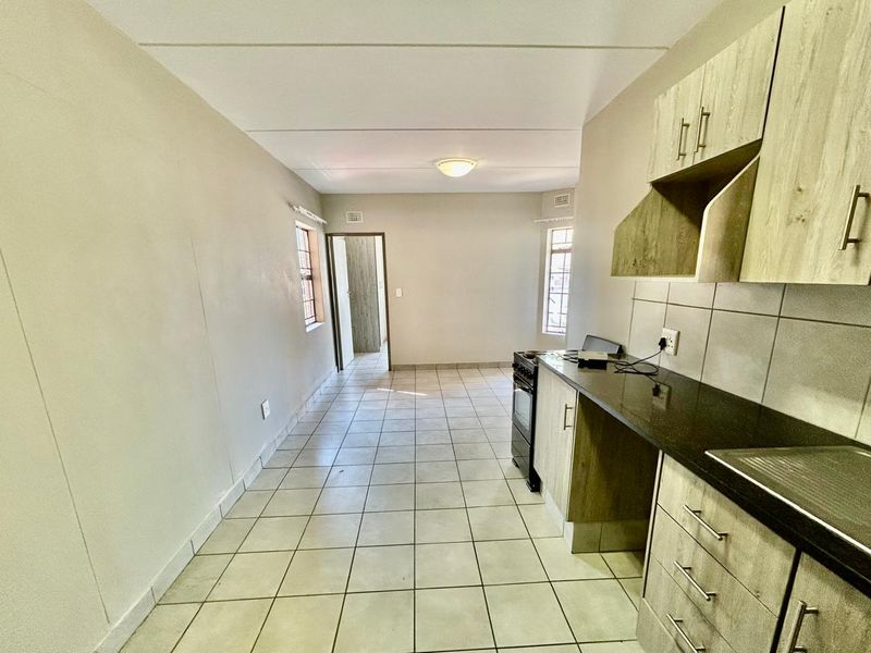 A functional kitchen featuring light wood-finish cabinetry, dark stone countertops, tiled flooring, and a built-in tiled backsplash, presented in a clean, empty space.