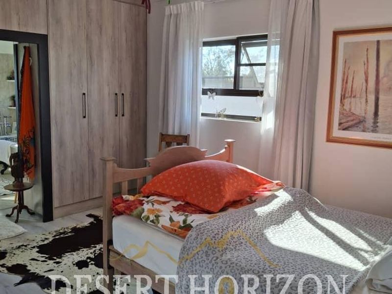 A well-maintained bedroom featuring built-in cupboards, laminate flooring, and a top-hung window, offering a functional and comfortable living space.