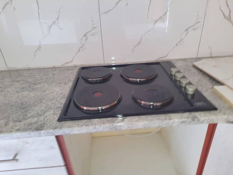A kitchen area featuring a black electric hob set into a granite countertop with marble-effect wall tiling and under-counter cabinetry.