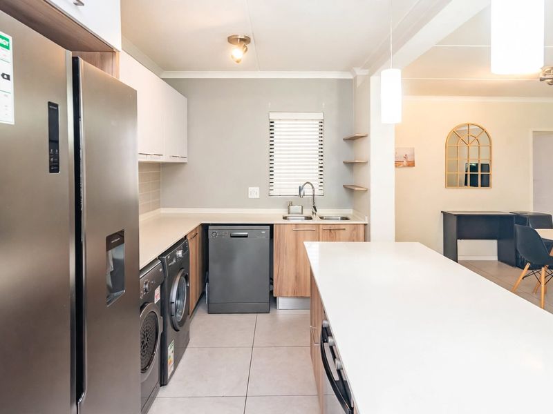 Modern open-plan kitchen featuring a central island, sleek cabinetry, tiled flooring, and integrated appliances, seamlessly flowing into the adjacent dining area.
