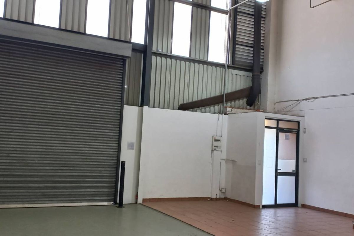 Industrial warehouse space featuring a high-clearance roller shutter door, mezzanine access staircase, and functional utility area with high ceilings.