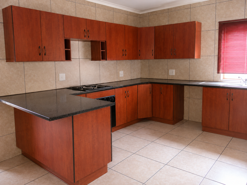 A functional kitchen featuring wood-look laminate cabinetry, granite countertops, an integrated electric hob and oven, and neutral ceramic tiling throughout.