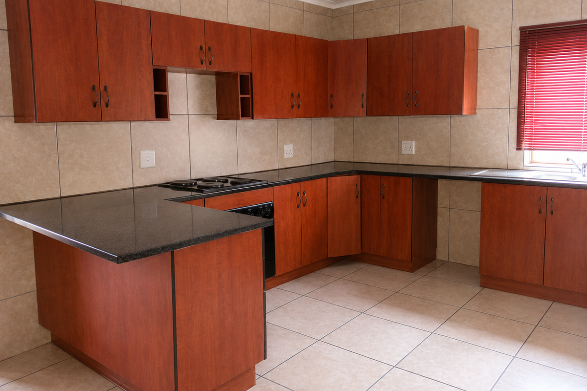 A functional kitchen featuring wood-look laminate cabinetry, granite countertops, an integrated electric hob and oven, and neutral ceramic tiling throughout.