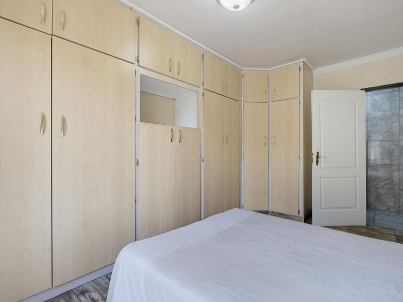 A bedroom featuring extensive light wood-finish built-in cupboards, tiled flooring, and a panel door leading to an adjacent tiled space.