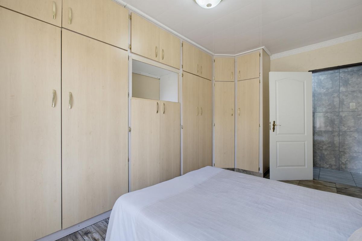 A bedroom featuring extensive light wood-finish built-in cupboards, tiled flooring, and a panel door leading to an adjacent tiled space.