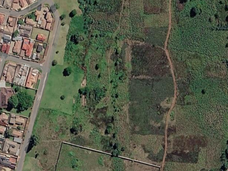 Aerial view of a vacant residential land plot showing surrounding vegetation, access tracks, and adjacent residential development.