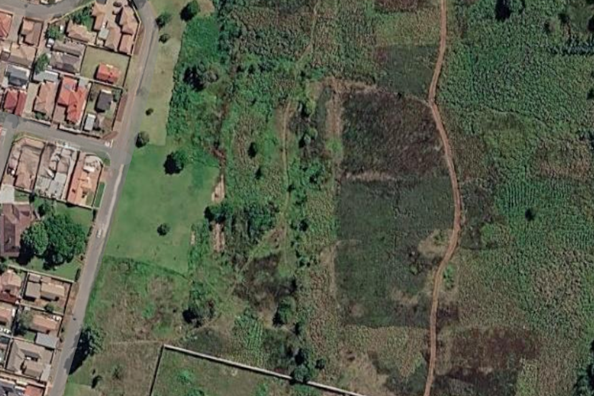 Aerial view of a vacant residential land plot showing surrounding vegetation, access tracks, and adjacent residential development.