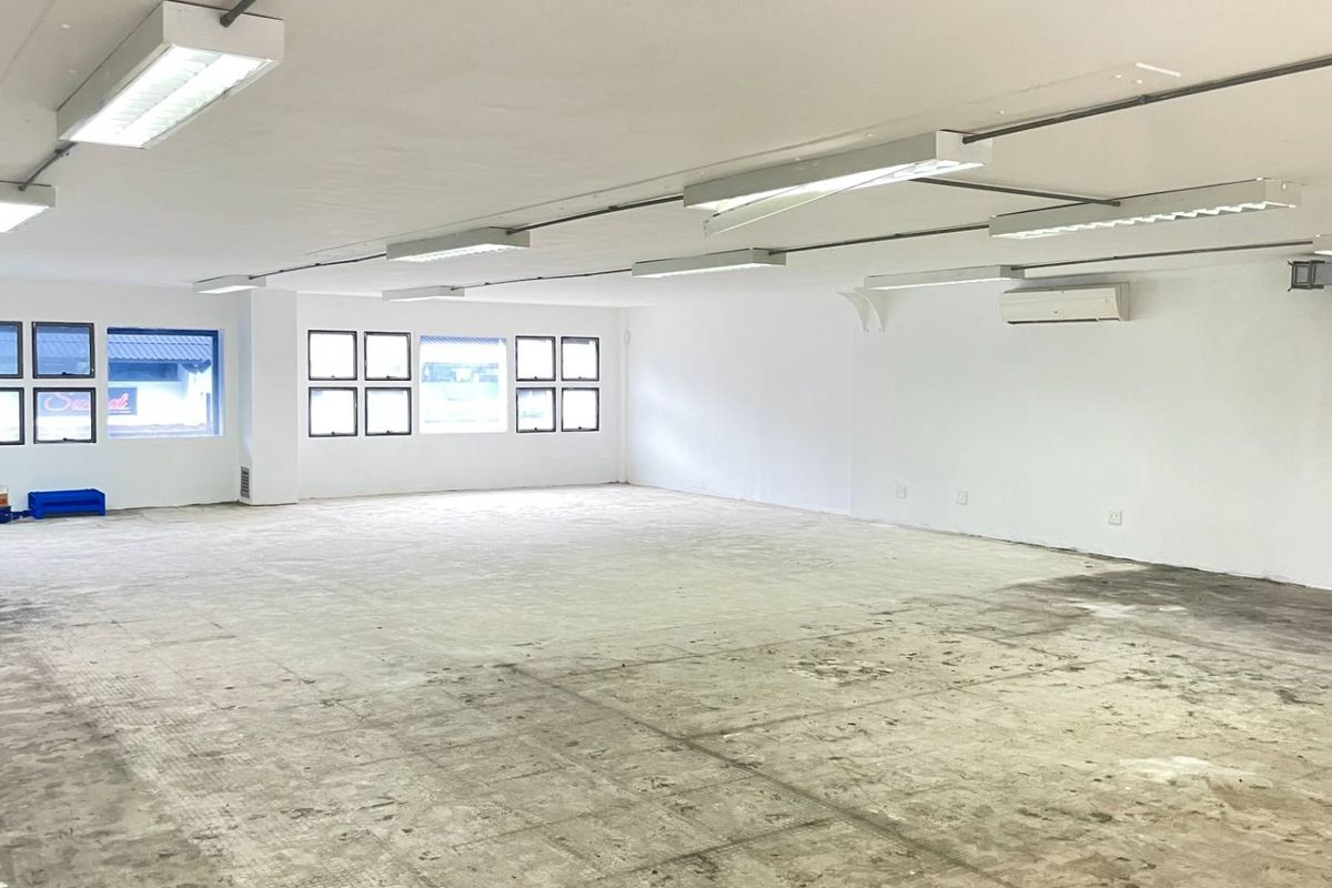 A spacious, open-plan retail or commercial unit featuring white walls, fluorescent lighting, air conditioning, and exposed concrete flooring ready for custom fit-out.