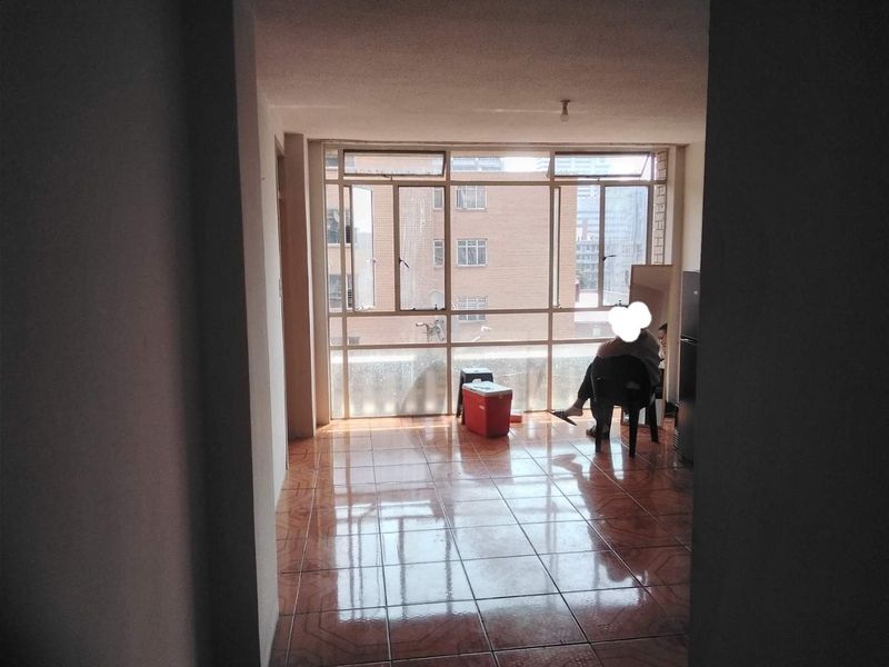 A bright living area featuring large windows with urban views and tiled flooring, offering a blank canvas for interior design.