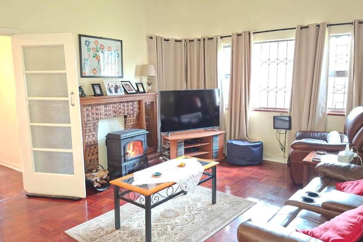 A cozy living room featuring classic parquet flooring, a built-in wood-burning fireplace, and large windows with security bars.