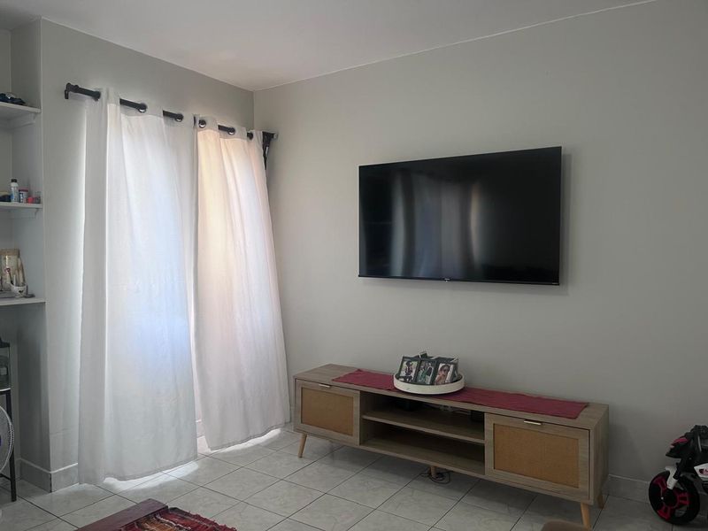 A bright living room area featuring neutral wall tones, tiled flooring, and a wall-mounted television setup.