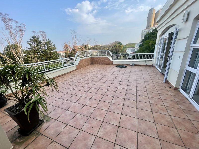 Spacious open-air balcony featuring tiled flooring and a metal balustrade, offering an expansive outdoor area accessible through double glass doors.