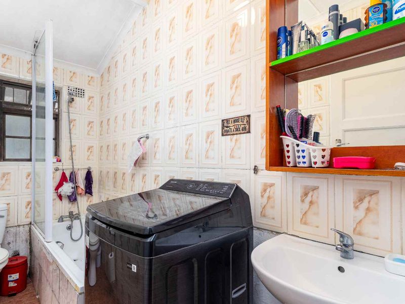 A dated bathroom featuring a bathtub with shower mixer, pedestal basin, and toilet, finished with patterned wall tiles requiring maintenance and updates.