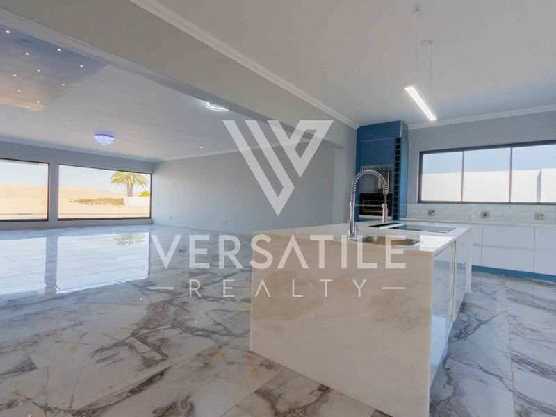 Spacious open-plan living and kitchen area featuring premium marble flooring, a large central island, and modern built-in appliances with abundant natural light.