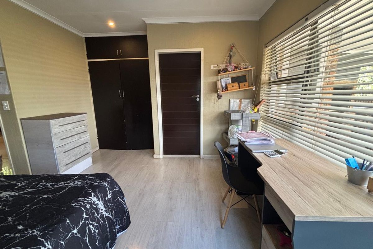 A bedroom featuring built-in cupboards, laminate flooring, and large windows with fitted blinds, providing a functional and well-lit living space.