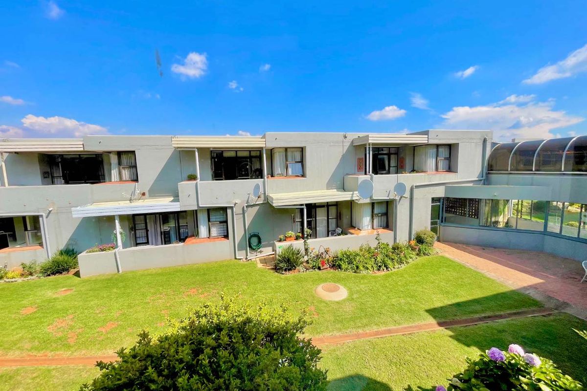 An elevated view of the apartment complex rear facade, featuring a shared garden, paved walkways, and multiple balcony access points.