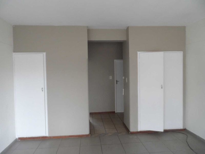 A neutral-toned hallway featuring tiled flooring and built-in storage cupboards, providing access to adjacent rooms within the apartment.