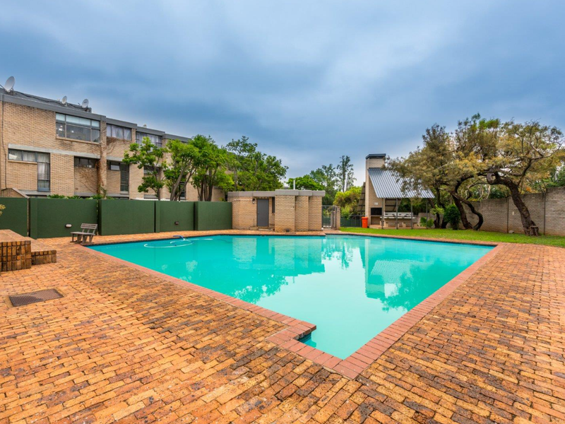 Communal pool area featuring brick paving, a built-in braai facility, and surrounding boundary walls within an apartment complex setting.
