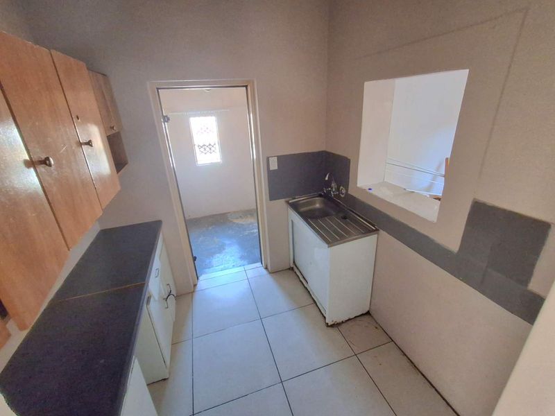 A functional scullery or utility area featuring built-in cabinetry, a stainless steel sink, and a convenient pass-through window to the adjacent living space.