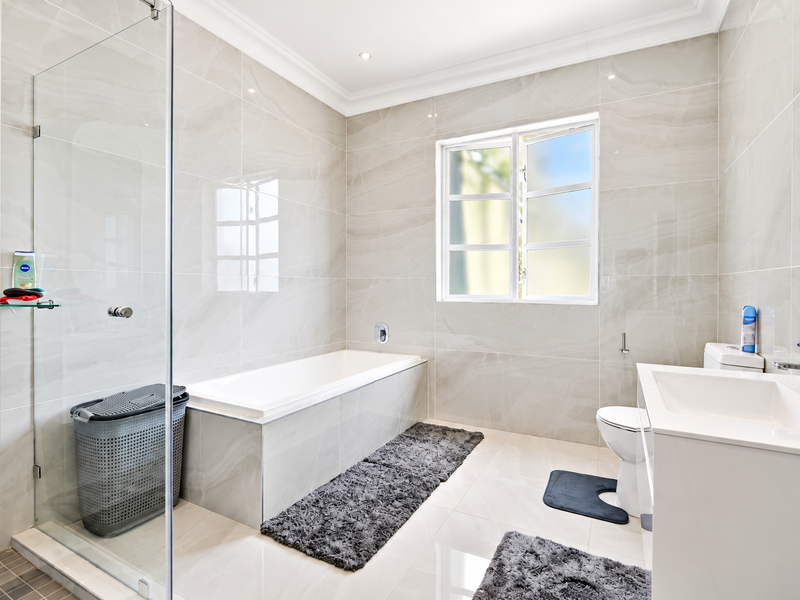 Modern bathroom featuring floor-to-ceiling marble-look tiling, a glass-enclosed shower, a built-in bathtub, and a sleek vanity unit.