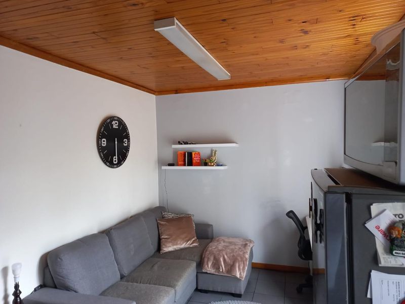 A living area featuring a timber tongue and groove ceiling, tiled flooring, and wall-mounted floating shelves.