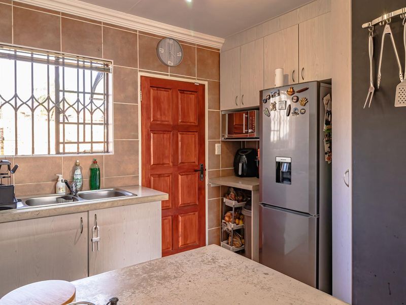 A functional kitchen featuring built-in cabinetry, a stainless steel sink, tiled backsplash, and a secure window with burglar bars.