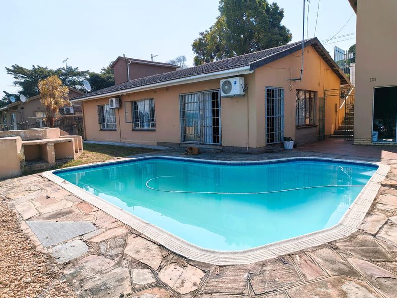 Outdoor pool area featuring a swimming pool, stone paving, and a built-in braai, set against the rear elevation of the house.