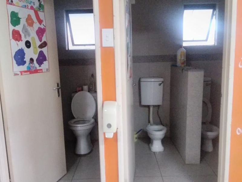 A functional bathroom facility featuring multiple toilet cubicles with tiled finishes and natural light from top-hung windows.