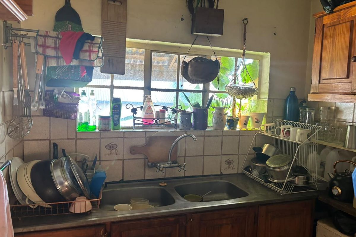A functional kitchen sink area featuring wooden cabinetry, a double bowl stainless steel sink, and tiled splashback, requiring cosmetic updates.