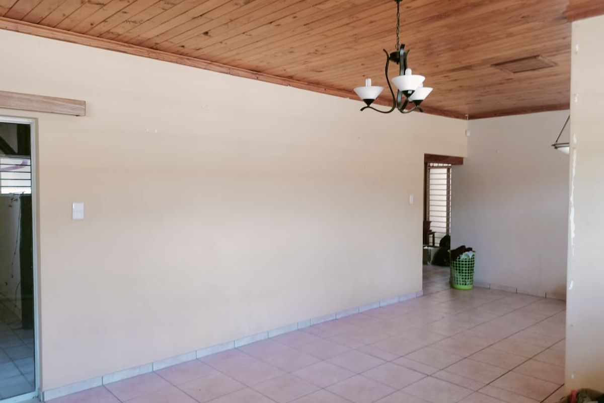 Spacious living area featuring a timber-clad ceiling, tiled flooring, and a central light fixture, offering a blank canvas for interior design.