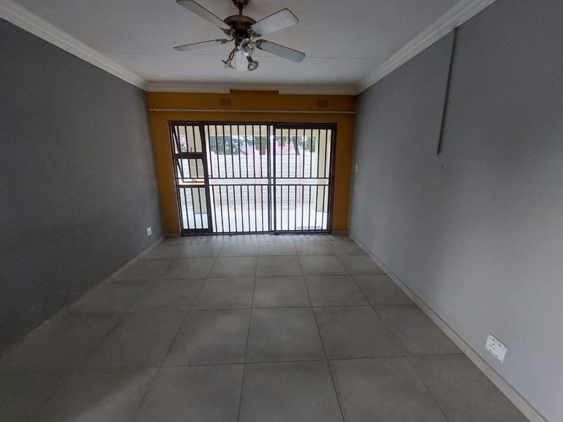 An empty living room featuring tiled flooring, a ceiling fan, and a sliding door with a security gate leading to the exterior.