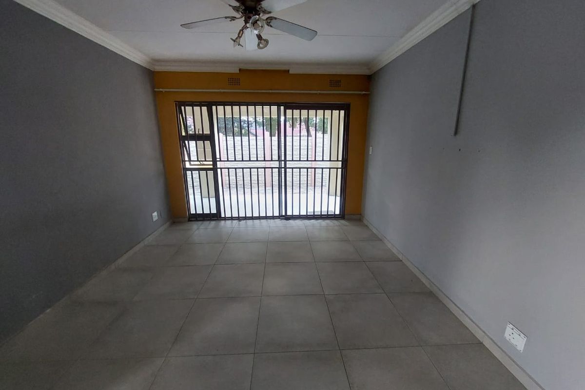 An empty living room featuring tiled flooring, a ceiling fan, and a sliding door with a security gate leading to the exterior.