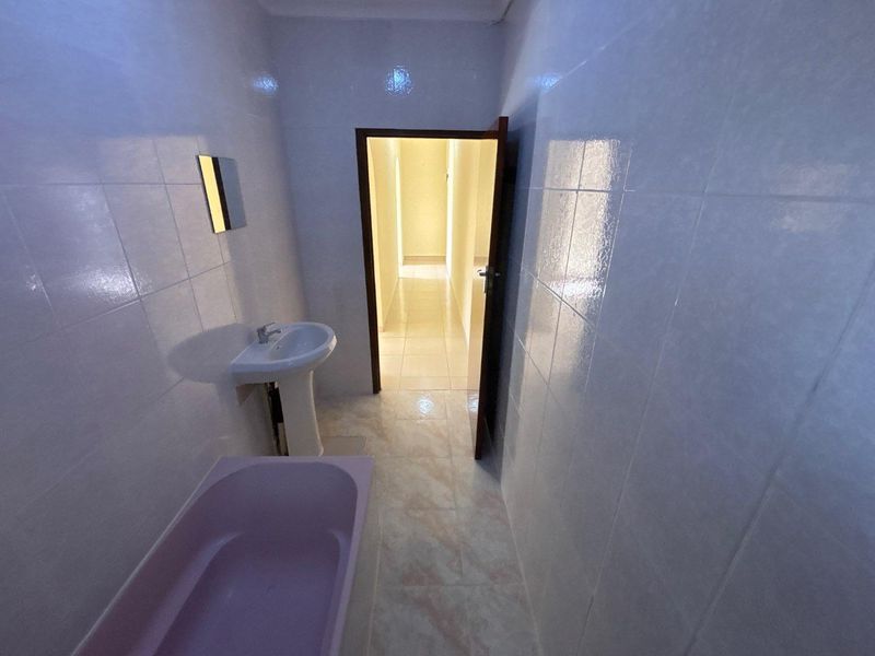 A compact bathroom featuring fully tiled walls, a pedestal basin, and a bathtub, presenting a dated aesthetic ready for modernization.