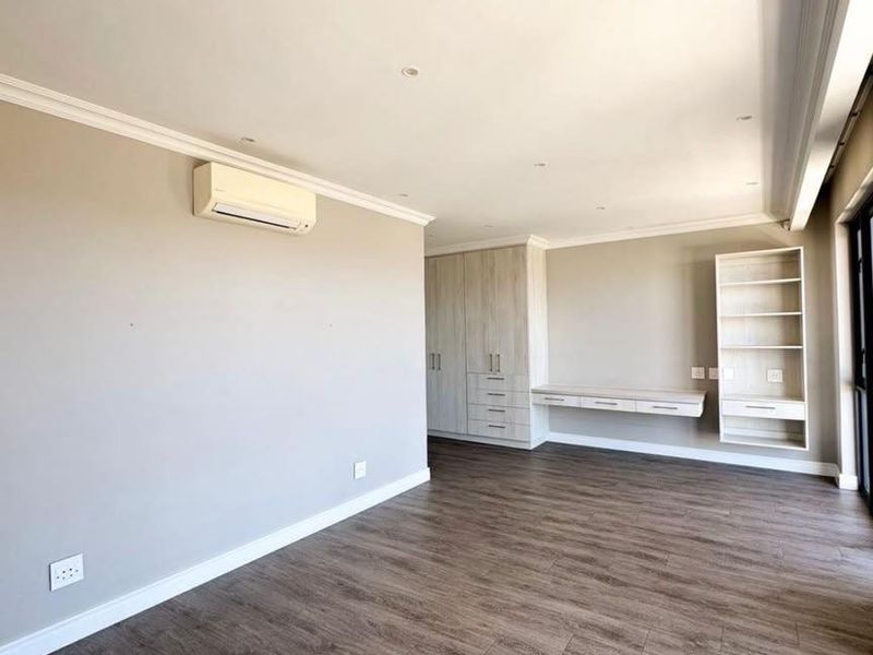 Spacious bedroom featuring modern laminate flooring, built-in cupboards, a floating desk, integrated shelving, and an air conditioning unit.