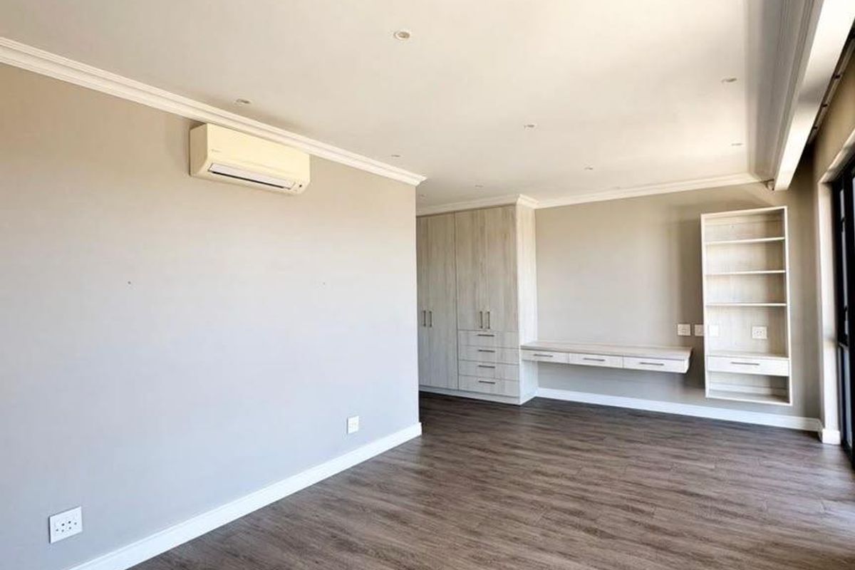 Spacious bedroom featuring modern laminate flooring, built-in cupboards, a floating desk, integrated shelving, and an air conditioning unit.