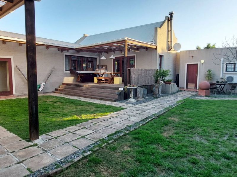 Rear exterior view featuring a timber deck with pergola, paved pathways, and a landscaped garden area with a water tank.