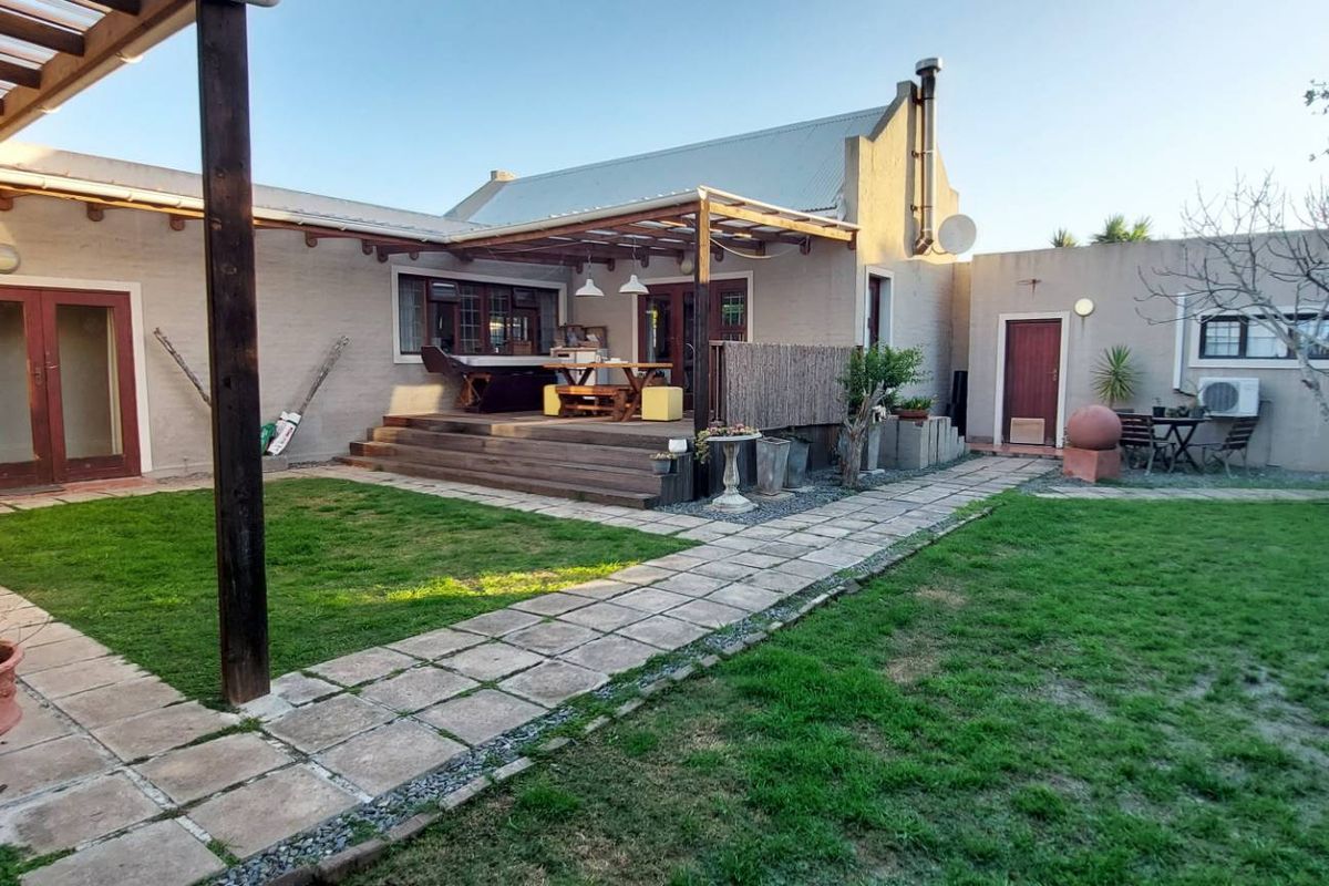Rear exterior view featuring a timber deck with pergola, paved pathways, and a landscaped garden area with a water tank.