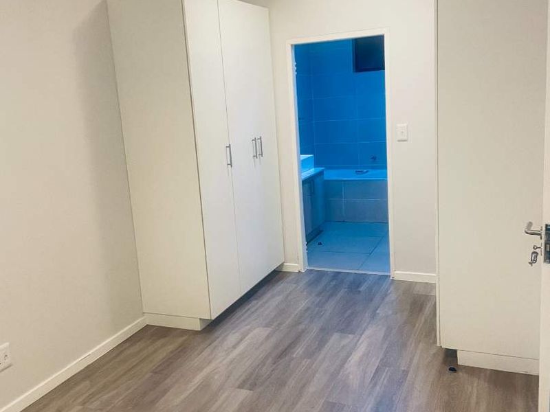 A clean, empty bedroom featuring modern laminate flooring and ample built-in cupboard storage, with direct access to an en-suite bathroom.